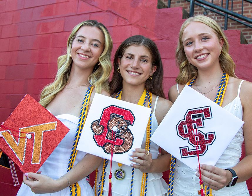  students hold up their decorated caps after graduation
